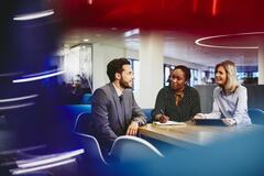 Business man and women in an office having a meeting. Primary colors: blue, red and turquoise.