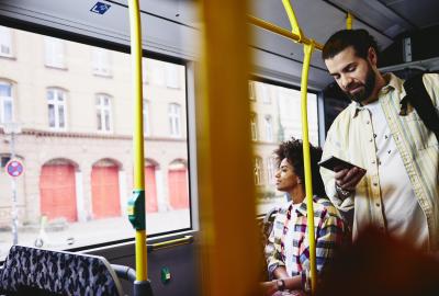 Man on his phone standing in a bus. Woman sitting down in the background. Man on his phone standing in a bus. Woman sitting down in the background.