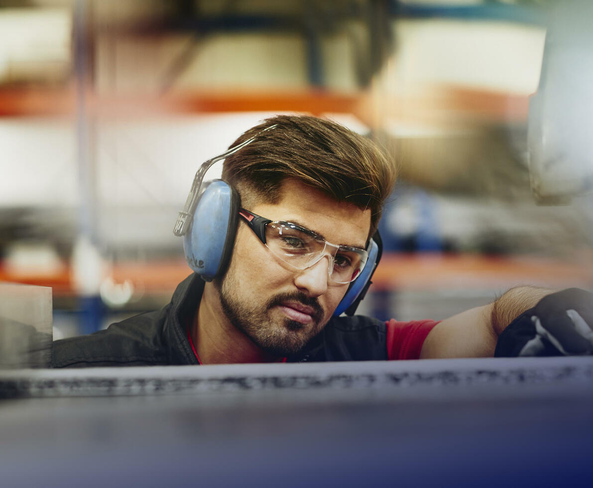 male wearing protective ear covers, safety gloves and safety glasses on a production site male wearing protective ear covers, safety gloves and safety glasses on a production site