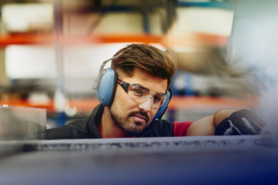 Randstad Operational Facharbeit & Handwerk male wearing protective ear covers, safety gloves and safety glasses on a production site