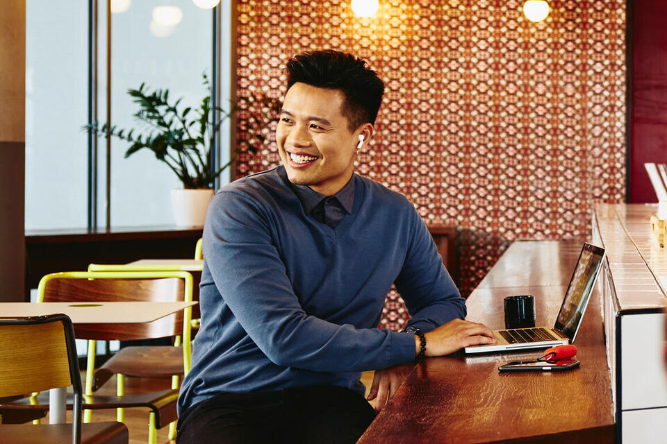 Randstad Professional male looking away sitting in a restaurant smiling with laptop.