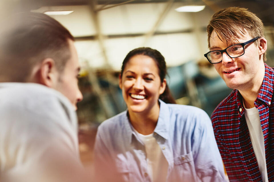 Randstad Professional Three people having a conversation in a warehouse, smiling.